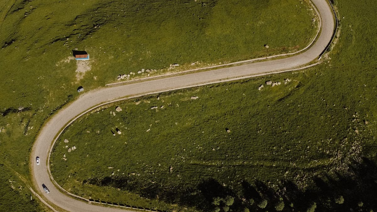 A scenic aerial shot of a winding road curving through lush green hills in summer.